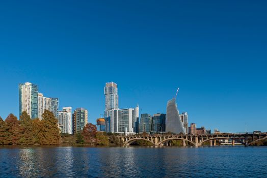 A vibrant city skyline with modern architecture reflecting in the river under clear blue skies.