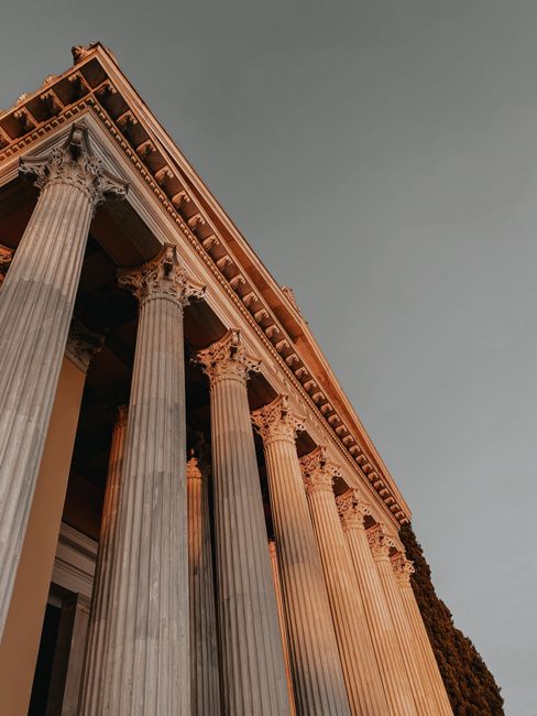Low angle view of classical building columns with intricate detailing against a gray sky.