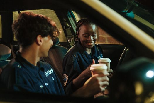 Two police officers enjoying a moment with coffee in their patrol car at night.