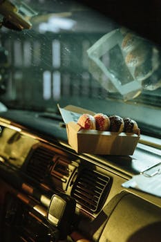 A box of assorted donuts placed on a car dashboard, highlighting indulgence and a sweet treat on the go.