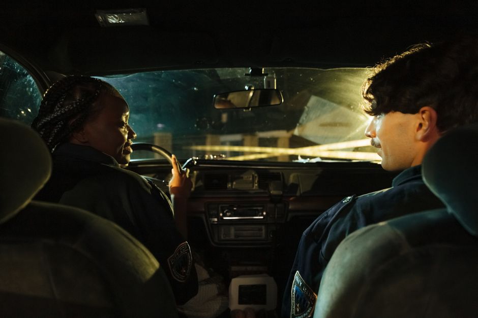 Two women sitting in a police car or talking to a police officer outside a restaurant at night looking shaken