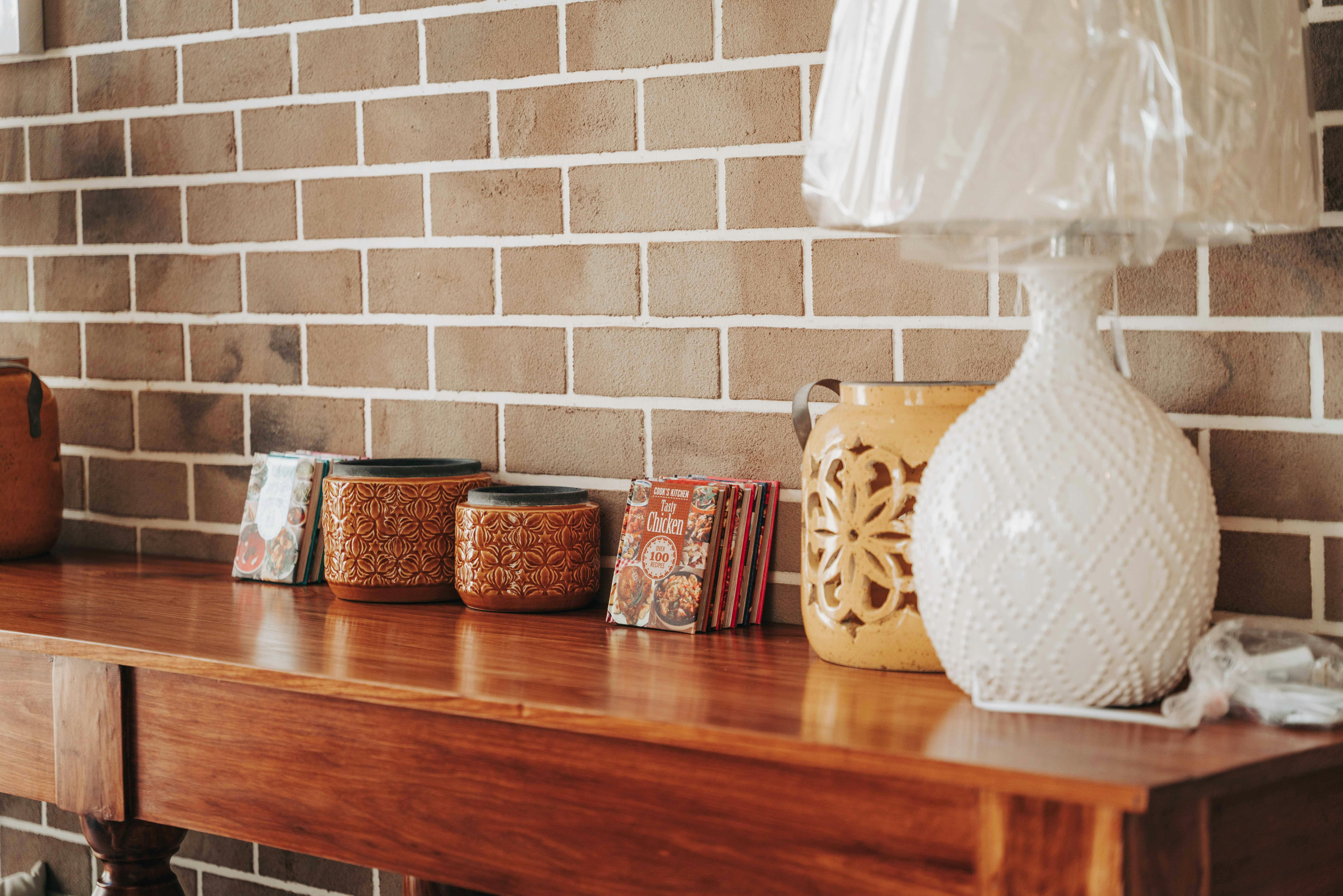 Rustic kitchen scene featuring a brick wall, wooden table, ceramic jars, and a decorative lampshade.