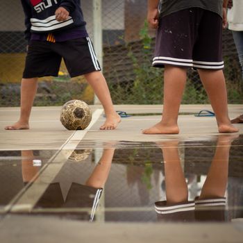 Children enjoy a playful soccer game on a wet court with reflections.（イメージ）