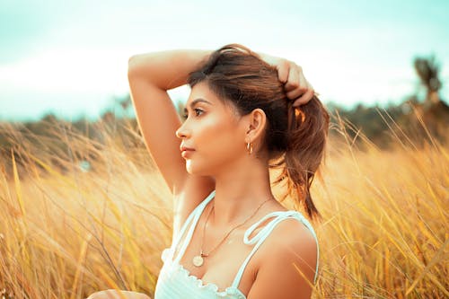 A Woman in White Tank Top Standing on Brown Grass Field
