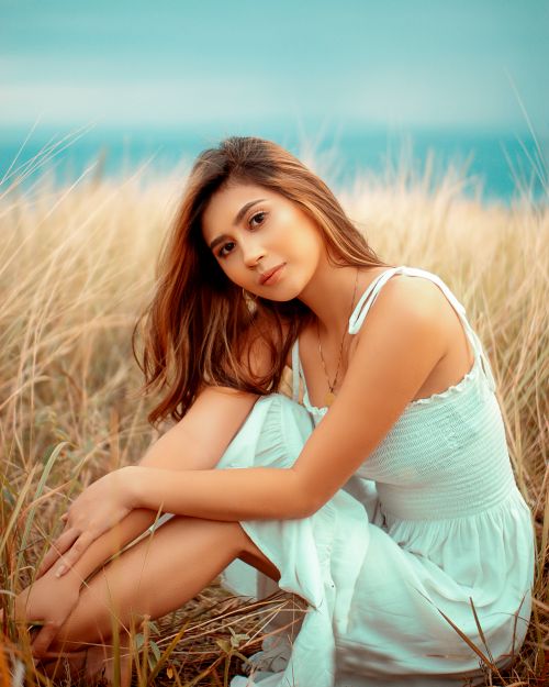 Free A serene portrait of a young woman in a white dress sitting in a grassy field. Stock Photo