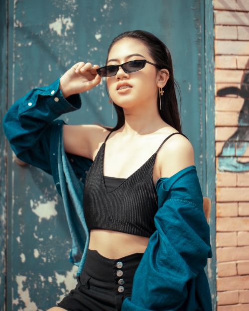 Free Chic young woman in sunglasses and crop top posing confidently outdoors against a textured wall. Stock Photo
