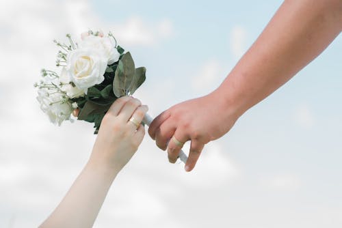 Persons Wearing Wedding Rings Holding a Flower Bouquet