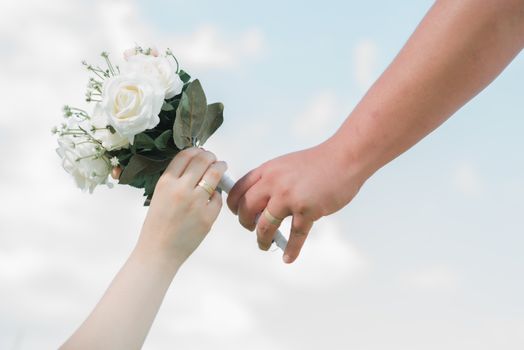 Close-up of hands exchanging wedding bouquet as a romantic gesture outdoors.
