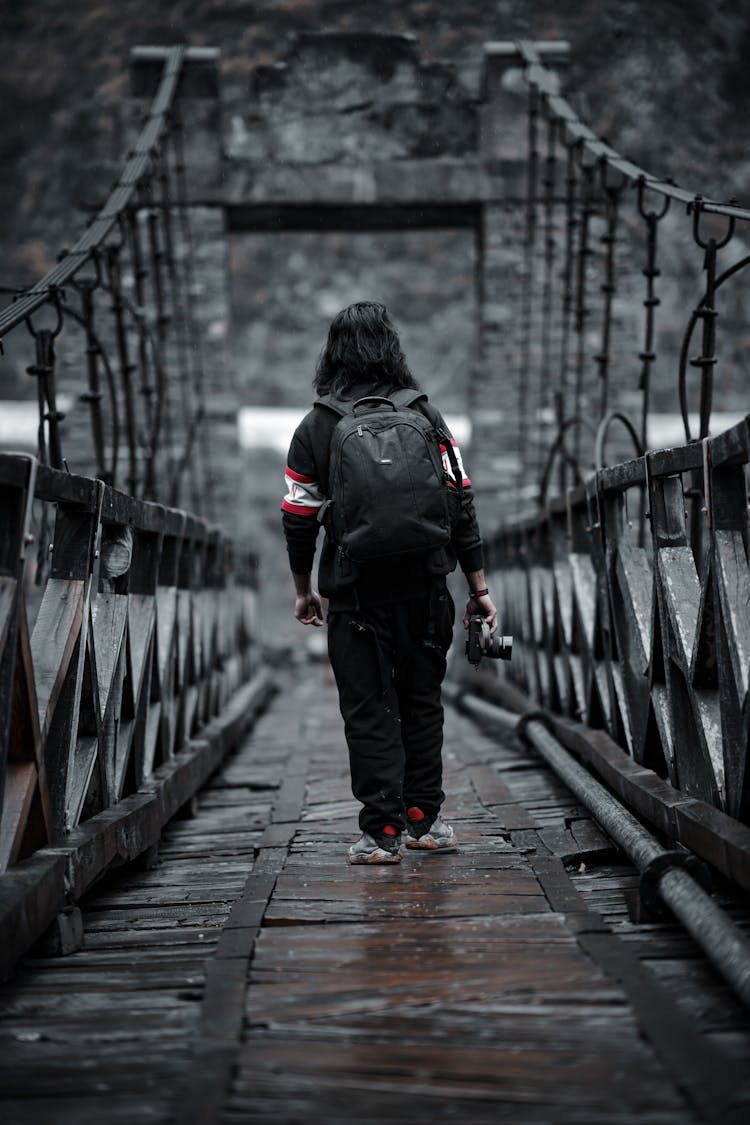 Man In Black Jacket And Pants Walking On Wooden Bridge