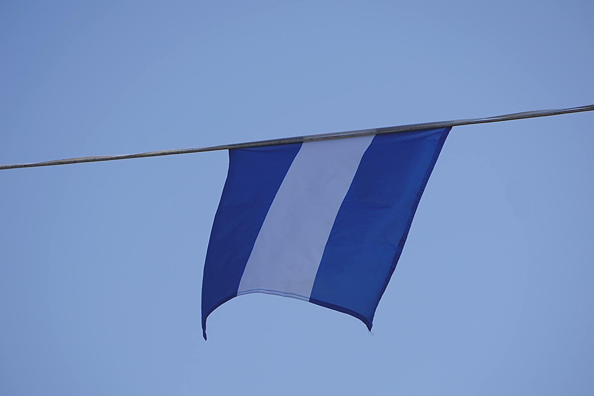 Close-up of a blue and white flag hanging under a clear blue sky, showcasing national pride.