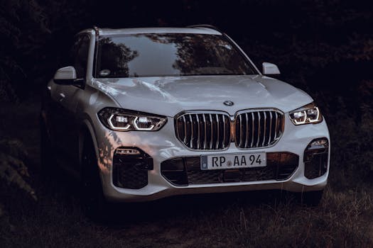 Captivating shot of a shiny white SUV with headlights on, parked outdoors with reflections of nature.