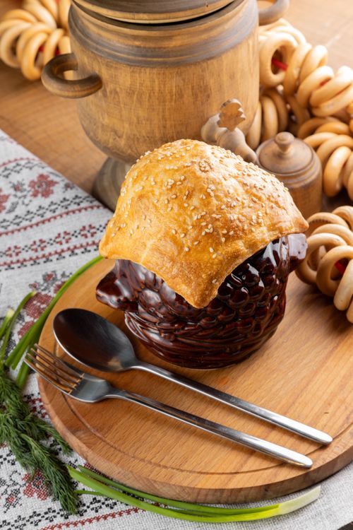 Free Traditional ceramic pot with bread topping, cutlery, and rural decor on a wooden board. Stock Photo