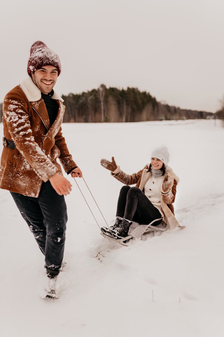 Man Towing Woman On Sleigh In Snow