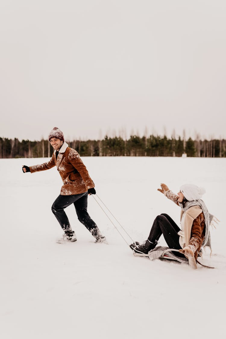 Man Pulling Girlfriend On Sledge In Winter Outdoor Scenery