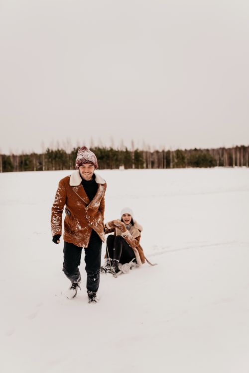 Free Couple enjoying a playful winter day with a sledge in a snowy field. Stock Photo