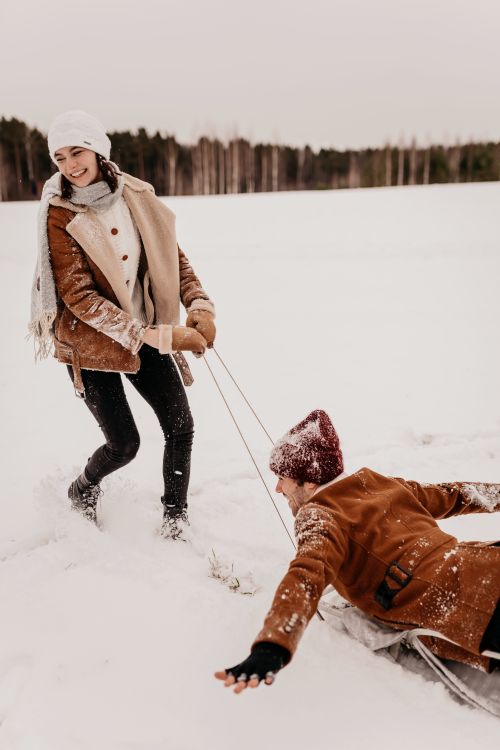 Free A couple having fun in the snow, pulling a sled on a wintry day dressed warmly. Stock Photo