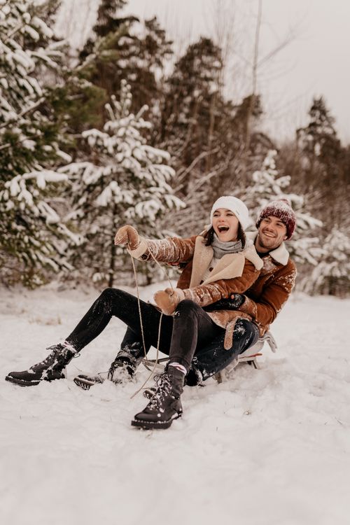 Free Joyful couple enjoying a snowy day sledding through a winter landscape, capturing fun and love. Stock Photo