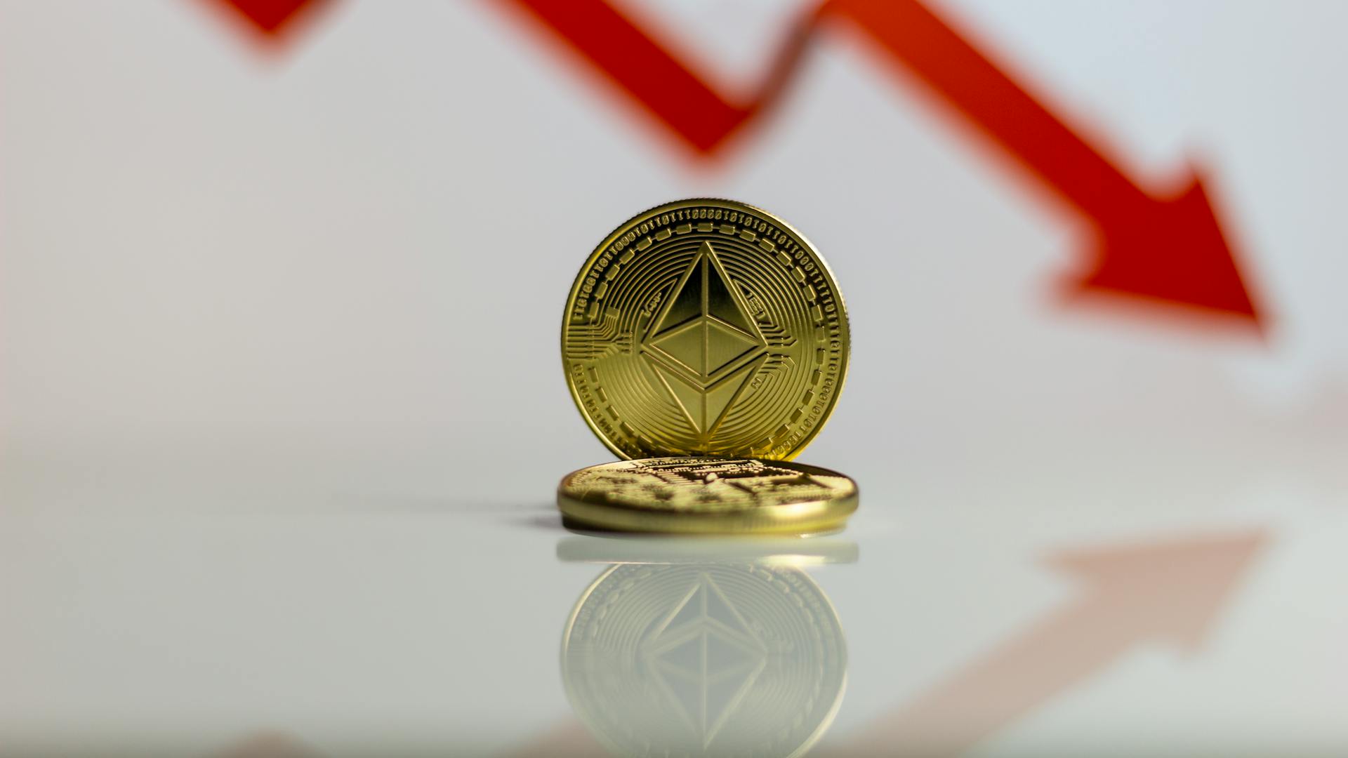 Close-up of Ethereum cryptocurrency with red downward arrow, symbolizing market decline.