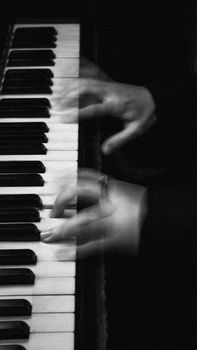 Blurry hands playing piano keys in a black and white artistic shot.