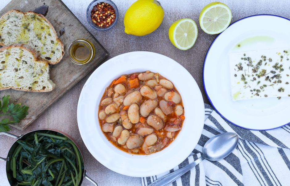 A bowl of cooked white cannellini beans next to a small dish of dried navy beans and a sprig of rosemary