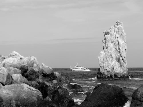 Grayscale Photo of White Ship on Sea Near Rock Formation