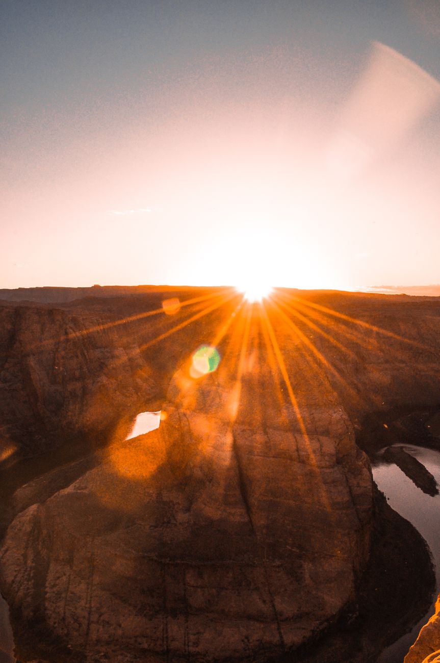 Captivating sunrise over Horseshoe Bend with sun rays illuminating the desert landscape.