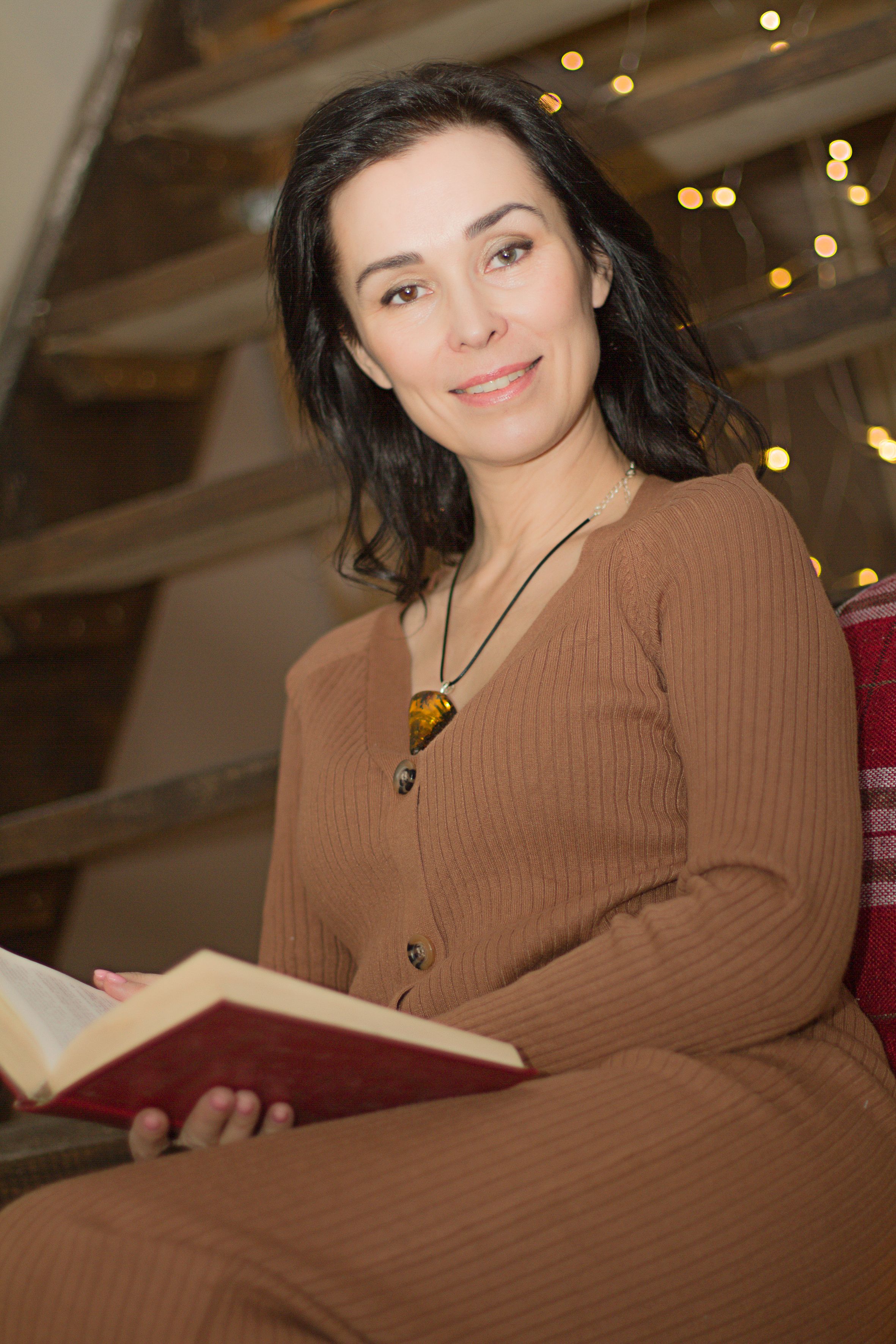 Woman in a cozy indoor setting, sitting and reading with a warm smile.