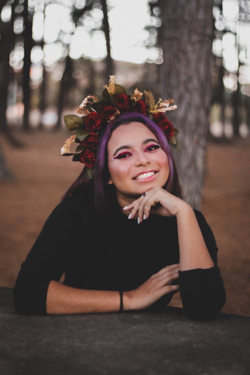 A Woman in Black Sleeves Wearing a Flower Crown Smiling with Her Hand on Her Chin