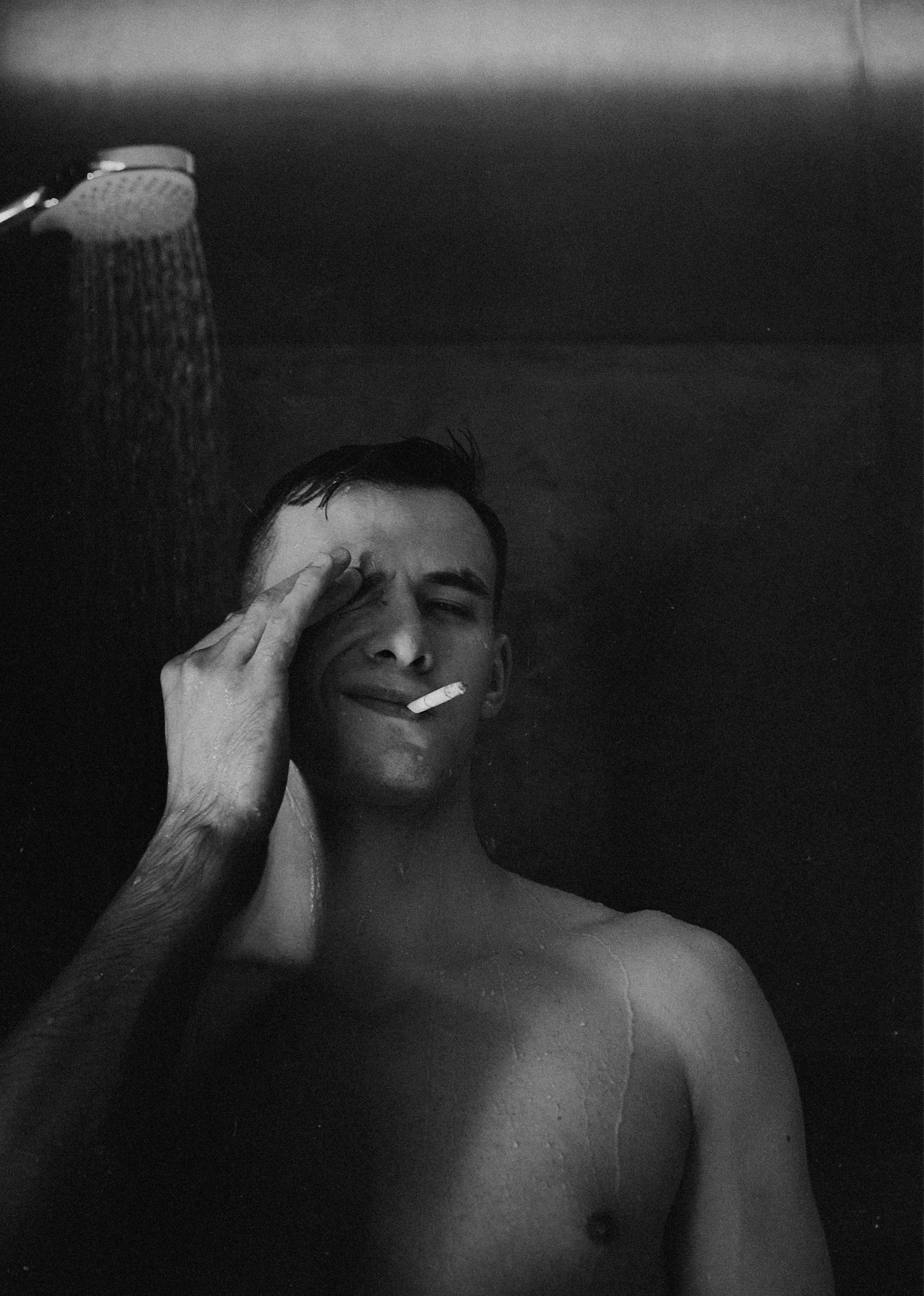 Black and white portrait of a man smoking in the shower with eyes closed, creating a moody atmosphere.