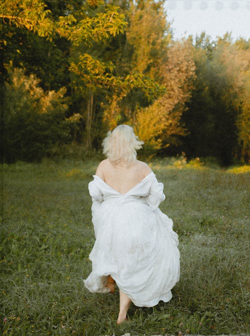 A Woman in White Dress Running on Green Grass Field