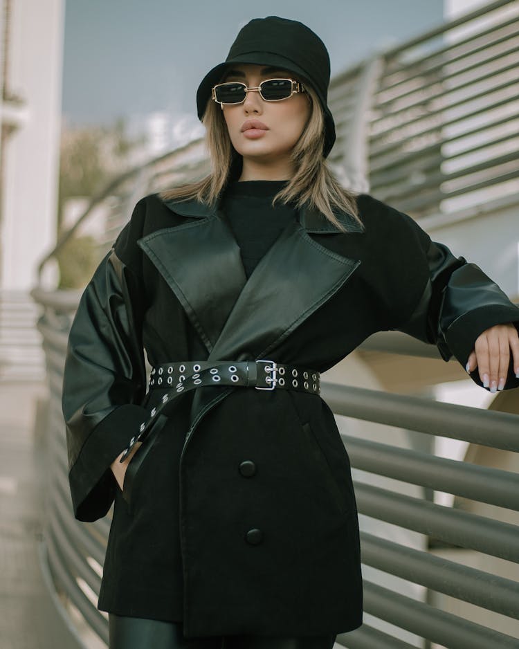 Female Model In Sunglasses Posing At Railing In Black Tailored Jacket And Hat