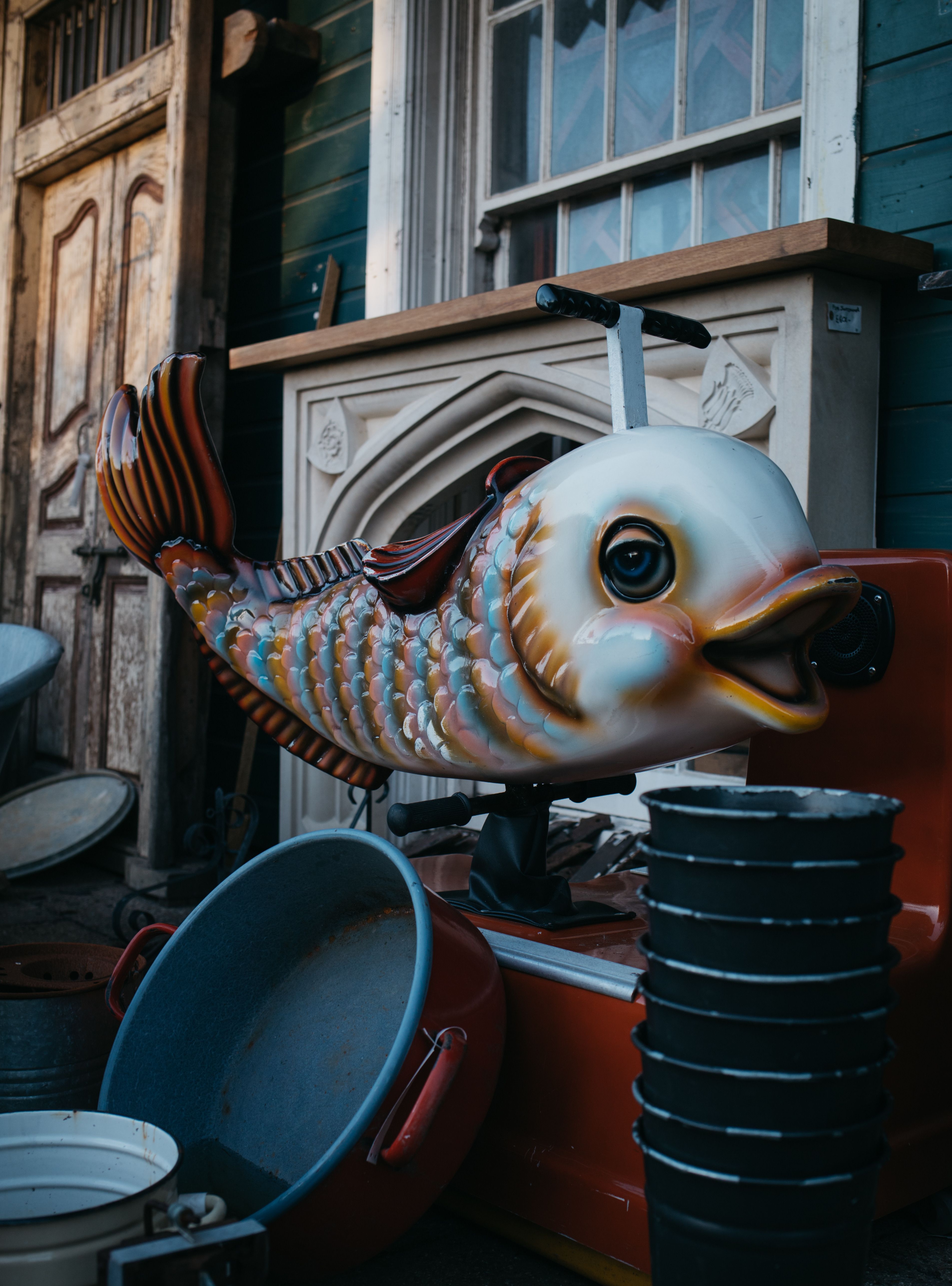 A vibrant fish amusement ride set against a backdrop of vintage wooden doors and eclectic decorations.