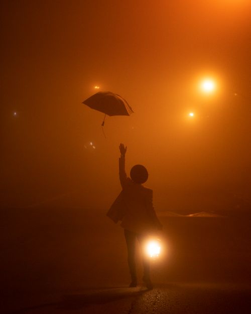 Free Silhouette of person reaching for umbrella in misty street with dramatic lighting. Stock Photo