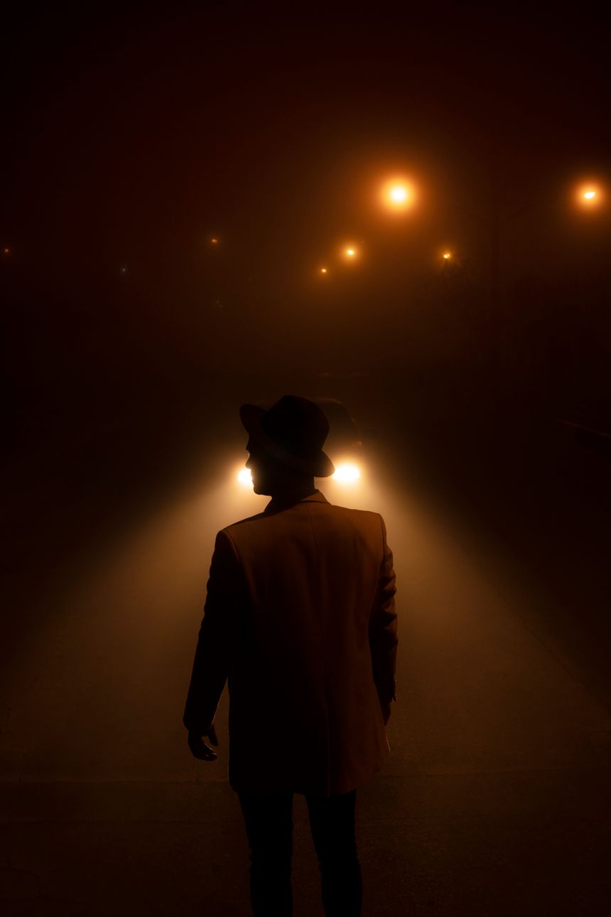 Silhouette of a man in a hat and suit in a foggy dim street — Ali Karimiboroujeni on Pexels