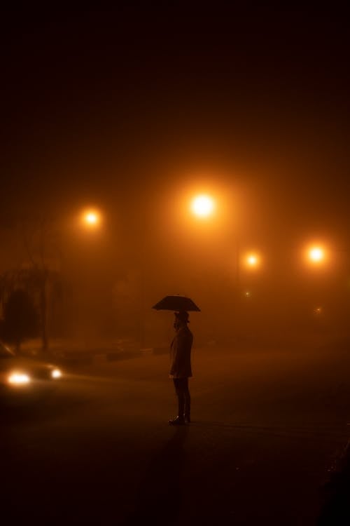 Person Standing on the Street at Night with Umbrella