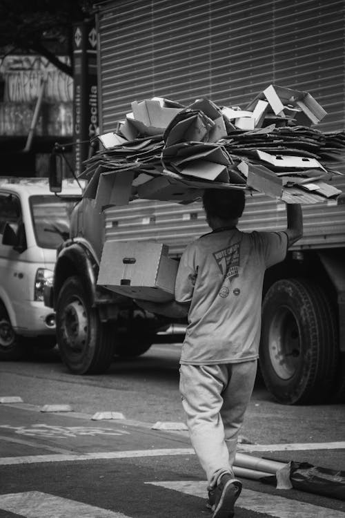 Grayscale Photo of a Man Carrying Cardboards