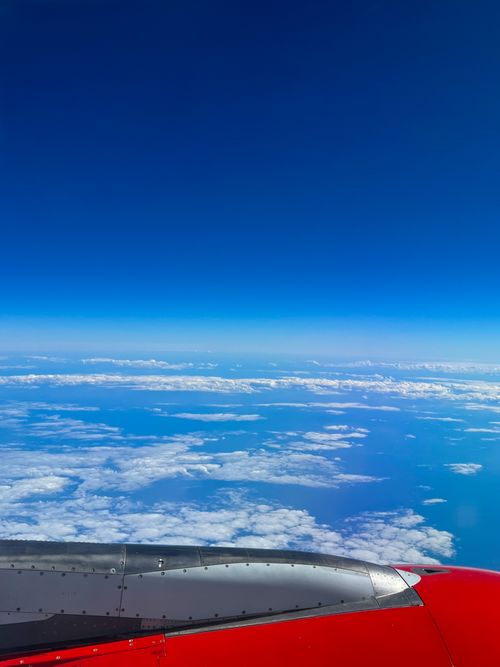 Free Stunning aerial view of clouds and ocean from airplane window with red wing. Stock Photo
