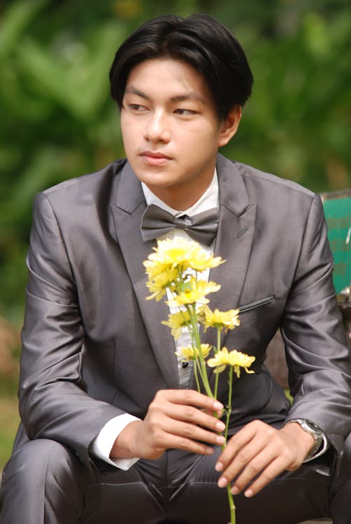 A Man in a Grey Suit Posing While Holding Flowers