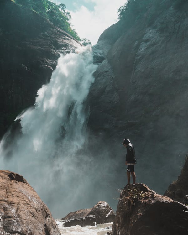 Free Man Standing on Brown Rock Cliff in Front of Waterfalls Photography Stock Photo