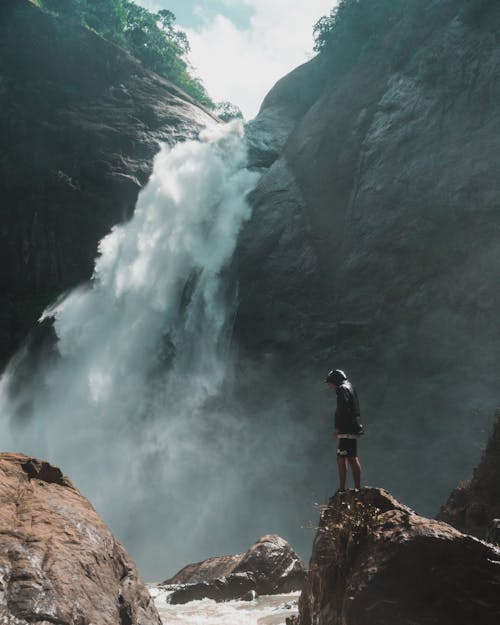 男子站在瀑布攝影前的棕色岩石懸崖上