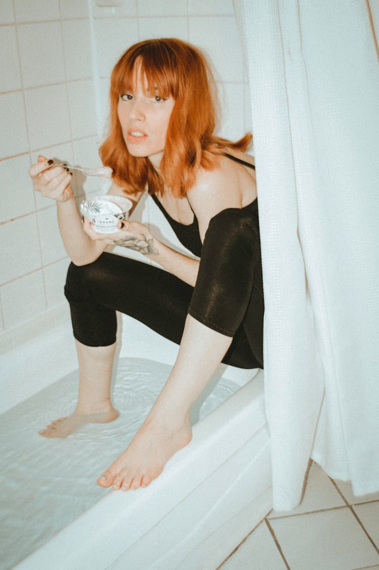 A Woman Sitting On A Bathtub Eating Yogurt