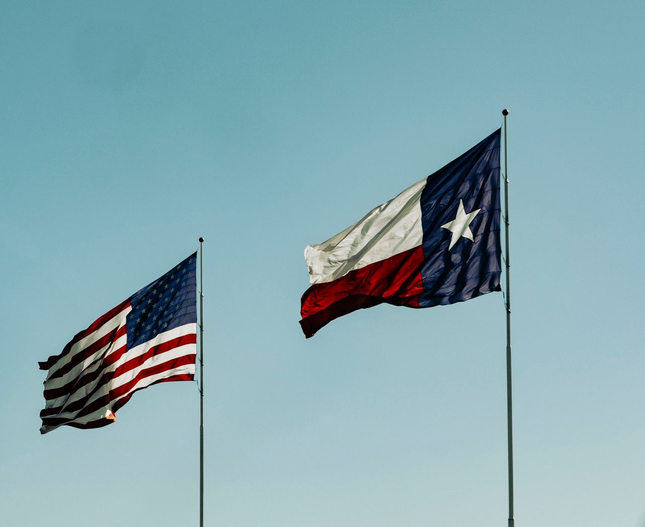 american and texas flags waving under a clear blue sky symbolizing pat