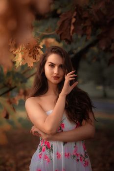 A serene portrait of a woman in a floral dress amidst autumn leaves, showcasing natural beauty.