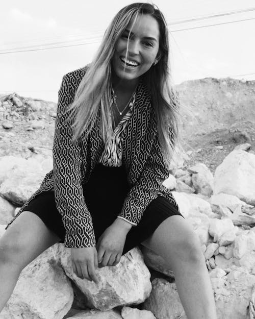 Grayscale Photo of a Happy Woman Sitting on Rocks