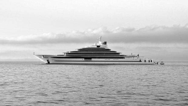 A sleek yacht cruising the calm ocean under a cloudy sky in monochrome beauty.