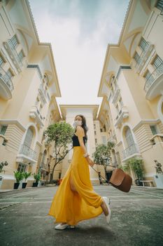 Stylish woman in yellow skirt and face mask walks in a beautiful courtyard.
