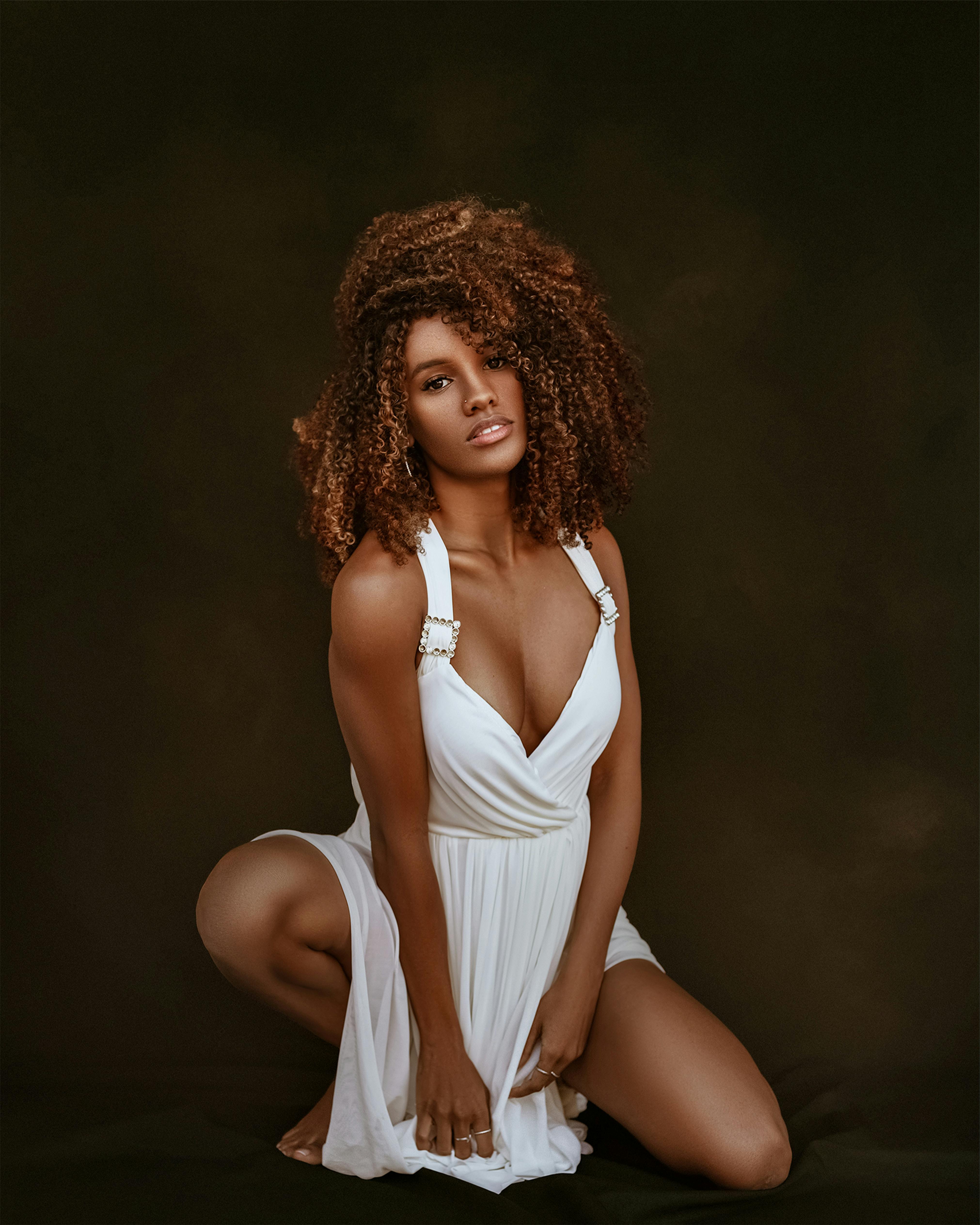 attractive woman with brown curly long hair crouching in white sexy dress