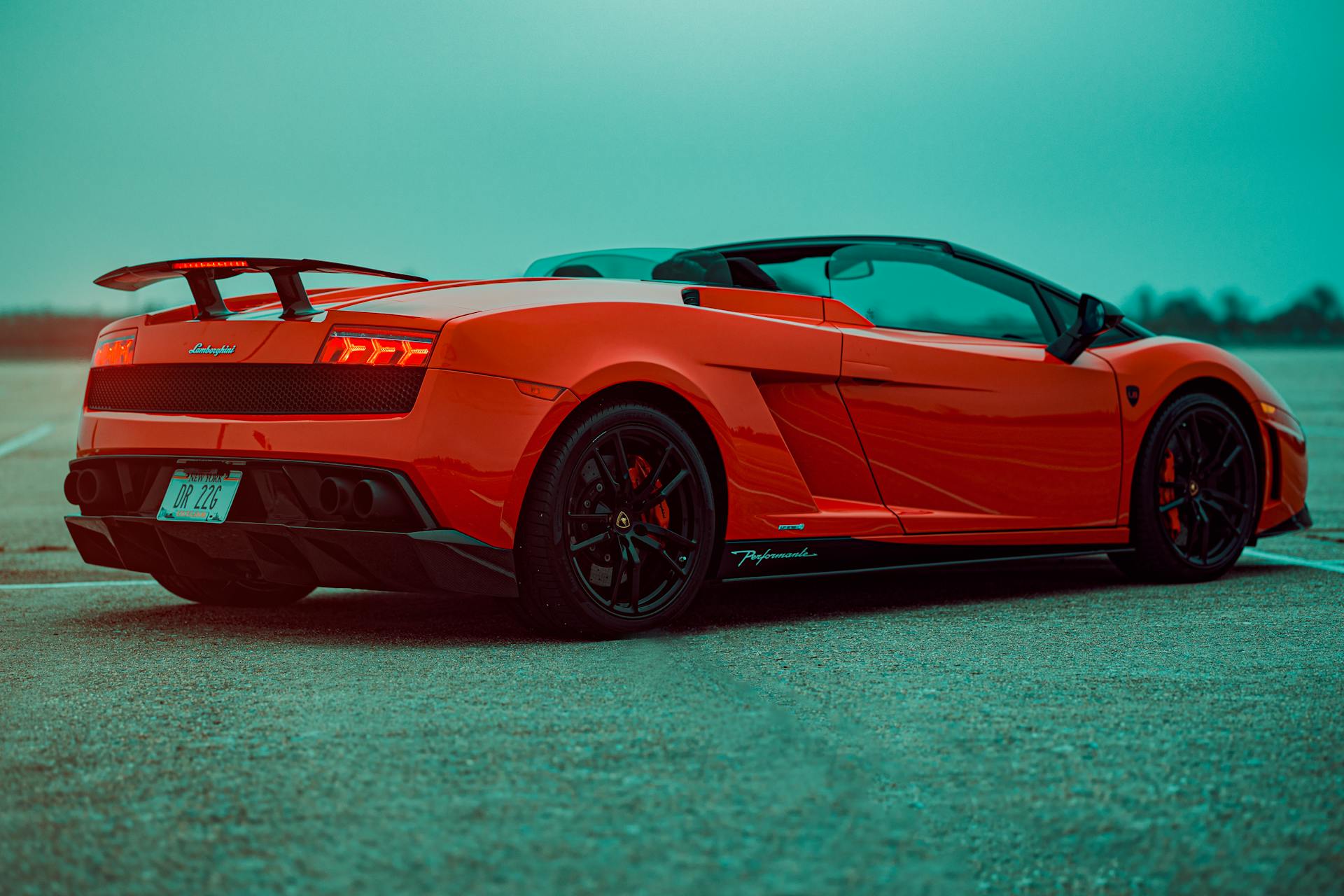 A sleek red Lamborghini convertible with a spoiler parked on an open road in New York, USA.