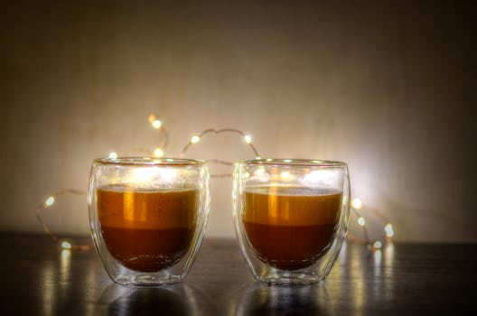 Two cappuccinos in double-walled glasses with festive lights.