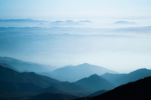 Free A tranquil scene of misty mountain ranges under a soft, blue sky at sunrise. Stock Photo